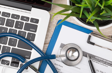 Close up view of doctor's desk with paperwork, computer and stethoscope