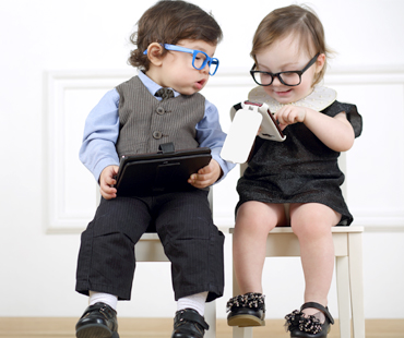 Two toddlers playing on tablet and smartphone